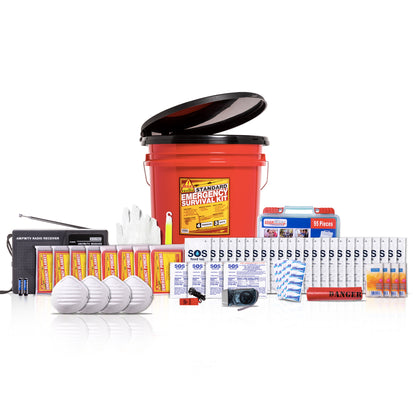 A survival emergency kit bundle arranged on a white studio background, centered around a large red plastic bucket with a black lid. Visible items include a radio, flashlights, white masks, gloves, bottled water, batteries, first-aid supplies, and other survival gear.