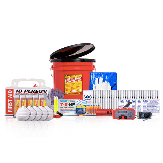A comprehensive emergency survival kit arranged on a white reflective surface. The kit includes a red plastic bucket with a black lid, a first aid package labeled '10 PERSON', several white cylindrical canisters, a blue box of gloves, a red and black digital thermometer, a yellow-and-blue T-5 NF tube, and other survival and safety items.