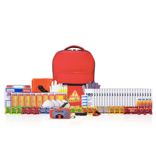 A comprehensive emergency preparedness and survival kit arranged neatly on a white background. The kit includes a bright red backpack, an orange emergency blanket, a red emergency whistle, a blue and orange personal locator beacon, multiple packs of instant noodles, bottled water, vitamins, first aid supplies, and other survival gear.